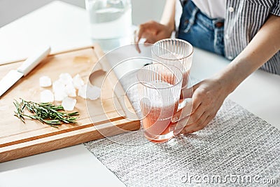 Close up of girl`s hands glasses with grapefruit detox diet smoothie rosemary and ice pieces on wooden desk. Stock Photo