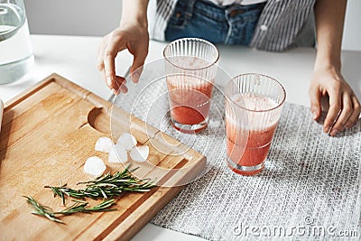 Close up of girl`s hands glasses with grapefruit detox diet smoothie rosemary and ice pieces on wooden desk. Stock Photo