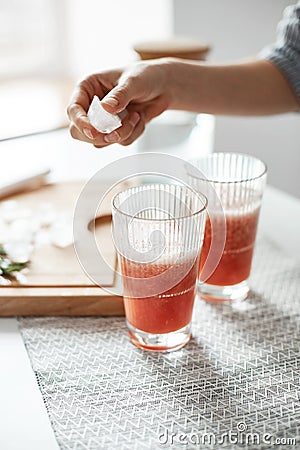 Close up of girl`s hands putting ice pieces in glasses with grapefruit detox healthy smoothie. Stock Photo