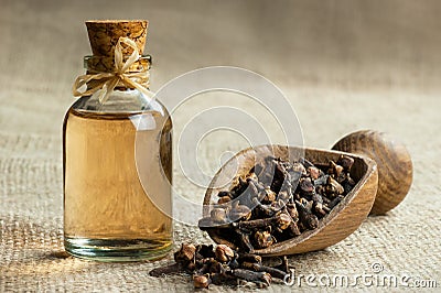 Close up glass bottle of clove oil and cloves in wooden shovel on burlap sack Stock Photo