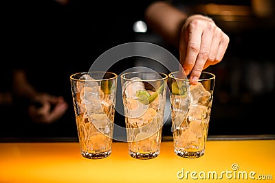 close-up of glasses with ice cubes in which hand of bartender puts cucumber slices Stock Photo