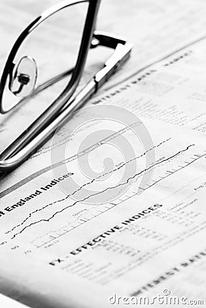 Close up of glasses and a newspaper showing financial charts. Stock Photo