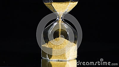 Close-up of golden hourglass. Stock footage. Stylish hexagon hourglass with falling gold specks on black isolated Stock Photo