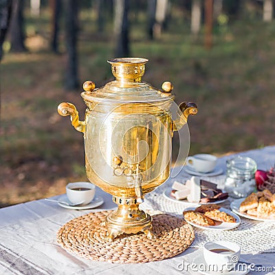 Golden russian samovar with tea cups and sweet snacks on table outdoor Stock Photo