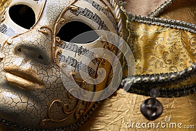 Close up of golden Venetian mask, fancy carnival mask with details and musical notes on golden surface Stock Photo