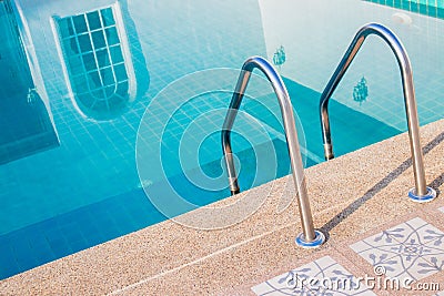 Close up grab bars ladder with blue water in swimming pool in the background. Stock Photo