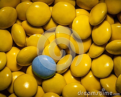 Close-up of a grayish-blue candy among bright yellow candies. Different not less. Stock Photo