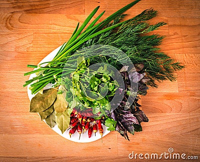 Close up of green organic herbs, basil, coriander, fennel, green onion, red chili peppers on white plate, rustic wooden background Stock Photo