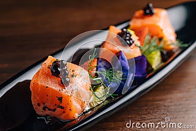 Close up Grilled Medium Rare Salmon Cube topping with caviar and served with strawberry and orange in black plate Stock Photo