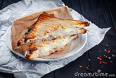 Close up on grilled sandwich with salmon and melted cheese and lettuce. Snack. Fast food for lunch. Sandwich served on white plate Stock Photo