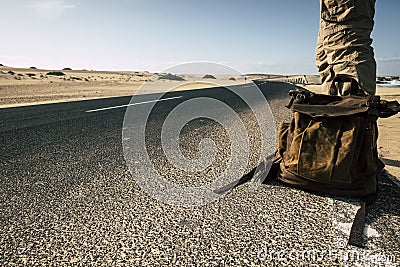 Close up ground point of view of man with leather backpack travel and wait for a car to share the trip together - sand and desert Stock Photo