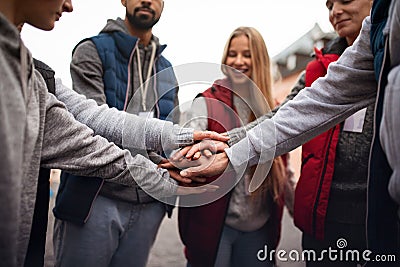 Close up of group of happy community service volunteers stacking hands together outdoors in street Stock Photo