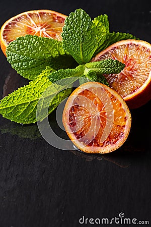 Close-up of half blood orange with mint on wet black slate, vertical Stock Photo