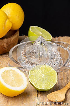 Close-up of half lemon, limes, wooden spoon, juicer and wooden bowl with lemons, black background, Stock Photo