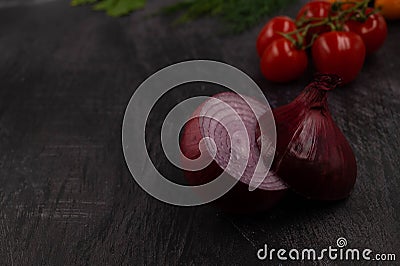 Close-up of a halved head of purple onion against a dark metal background with cherry tomatoes behind Stock Photo