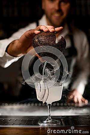 Close-up of hand of bartender holds piece of coconut and pours coconut milk into glass Stock Photo