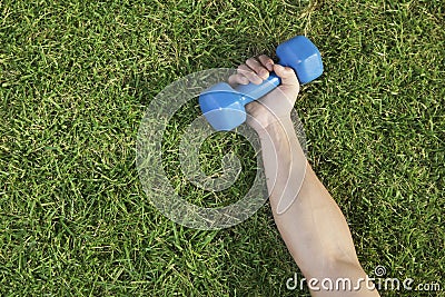 Close Up on Hand Holding Blue Dumbbell in Grass Stock Photo