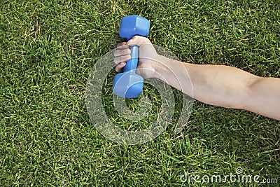 Close up on hand holding blue dumbbell in grass, view from above Stock Photo