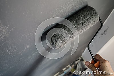 Close up of hand holding paint roller applying grey paint on wall. Stock Photo
