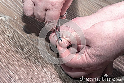 Close-up of a hand holding a scissors for cutting nails on toes on a wooden background at home. Stock Photo