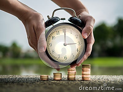 Close up hand holding time with stack of coins, time value of money concept in business finance theme. Saving money for future Stock Photo