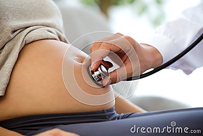 Hand of male obstetrician doctor with stethoscope listening to pregnant woman baby heartbeat. Stock Photo