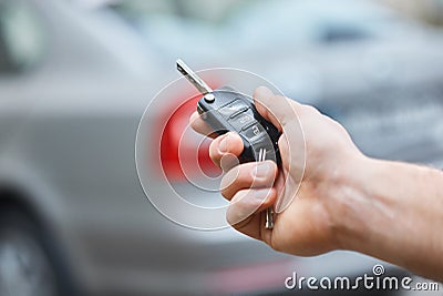 Close up hand of Man holding car key with blurred car on background. hand presses on the remote control car alarm systems. Stock Photo