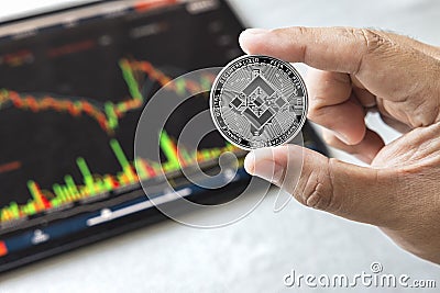 Close-up hand of man holding crypto coin on chart in tablet background. Blockchain technology finance future. Male hold BNB. Editorial Stock Photo
