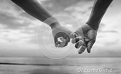 Close up hand of senior couple hook each other's little finger together near seaside at the beach,black and white picture Stock Photo