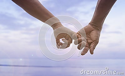 Close up hand of senior couple hook each other's little finger together near seaside at the beach,filtered image Stock Photo