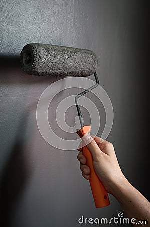 Close up of hand using paint roller applying grey paint on wall. Stock Photo