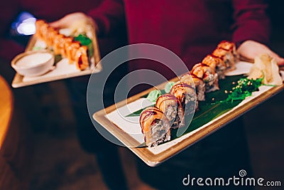 Close-up Hand Waiter holding Set Delicious fresh Sushi slate plate Sushi Rolls Warm Sake Unagi, Japanese raw fish in traditional Stock Photo