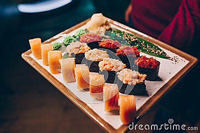 Close-up Hand Waiter holding Set Delicious fresh Sushi slate plate Sushi Rolls Warm Sake Unagi, Japanese raw fish in traditional Stock Photo