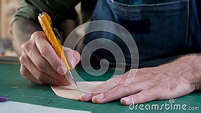 Close-up handcrafted leather worker sits cowhide with cutter according pattern drawn on leather, meticulous for beautiful Stock Photo