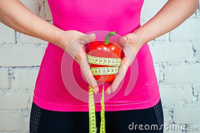 Close-up hands of a beautiful and young brunette woman holding a vegetable pepper and a measuring tape on a white brick Stock Photo