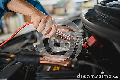 Close-up hands of a car mechanic holding the battery jumper wire. He uses battery jumper cables to charge a dead battery Stock Photo