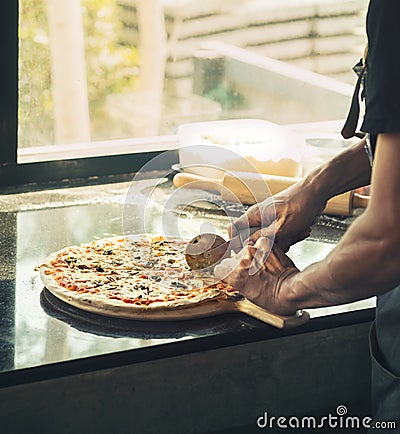 Close up of hand Chef black shirt cutting freshly baked pizza Stock Photo