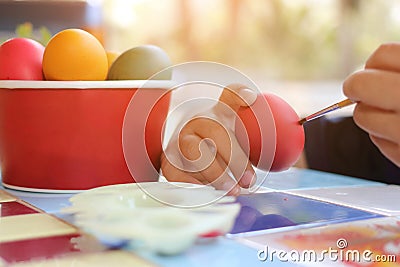 Close up hands of child coloring eggs with paintbrush for preparing Easter day on nature blurred background. Sunshine effect. Stock Photo