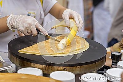 Close-up of hands of cook in gloves preparing Crepe, pancake with fresh banana. Healthy fresh food. Concept national Stock Photo