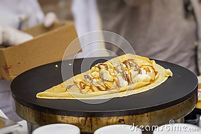 Close-up of hands of cook in gloves preparing Crepe, pancake on frying pan with fresh banana, sweet sauce, nutella Stock Photo