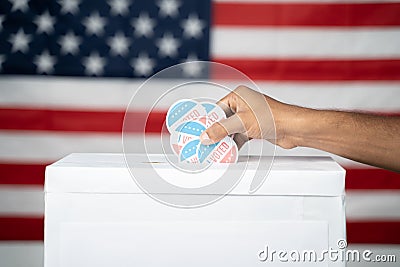 Close up of Hands dropping multiple I Voted sticker inside Ballot box with US flag as background, Concept of fraud in Stock Photo