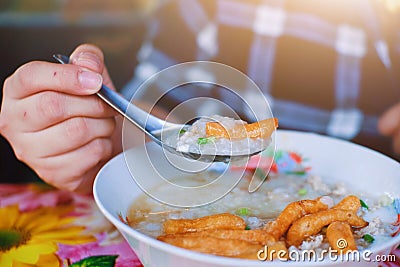 Close up Hands holding spoon with Congee or Rice porridge and deep-fried dough stick, egg ,minced pork balls in bowl Stock Photo