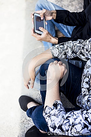 Close up of only hands and legs of teenager sitting on a wall and using smart phones and spending time with friends. Stock Photo