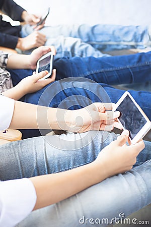 Close up of only hands and legs of teenager sitting on a wall and using smart phones and spending time with friends. Stock Photo