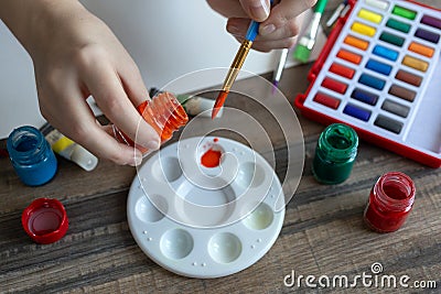 Close up of hands mixing colorful watercolor set and palette close up on wooden desk, art workplace. Top view. Stock Photo