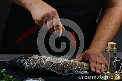 Close-up Hands in the process cooking fish with lemon juice. carp fish with various ingredients lemon, herbs and spices on shale b Stock Photo
