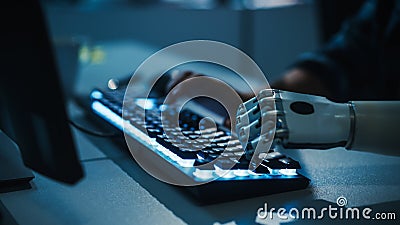 Close-up on Hands: Programmer With Disability Using Prosthetic Arm to Work on Computer Keyboard Stock Photo