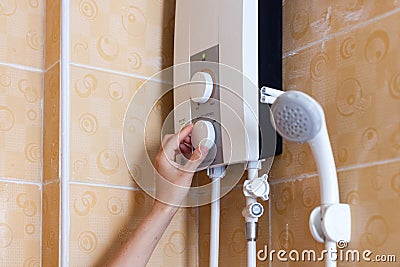 Close-up of hands setting the temperature of water in electric boiler in the shower room. Stock Photo