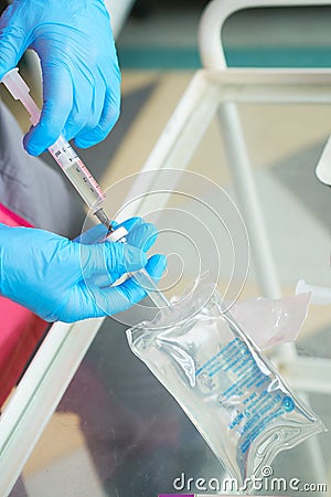 Close-up hands of young woman doctor anesthesiologist dressed in pink gown, blue gloves prepares solution for anesthesia Stock Photo