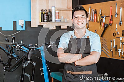 close up of handsome bicycle mechanic in smiling apron holding bicycle with crossed hands Stock Photo